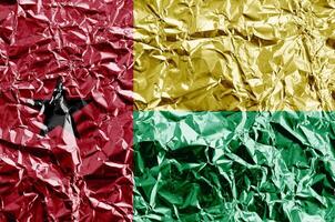 Guinea Bissau flag depicted in paint colors on shiny crumpled aluminium foil closeup. Textured banner on rough background photo