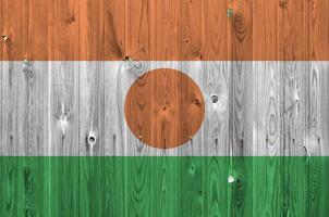 Niger flag depicted in bright paint colors on old wooden wall. Textured banner on rough background photo