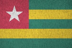 Togo flag depicted in bright paint colors on old relief plastering wall. Textured banner on rough background photo