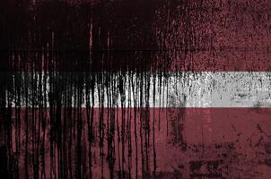 Latvia flag depicted in paint colors on old and dirty oil barrel wall closeup. Textured banner on rough background photo