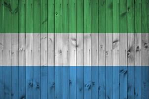 Sierra Leone flag depicted in bright paint colors on old wooden wall. Textured banner on rough background photo