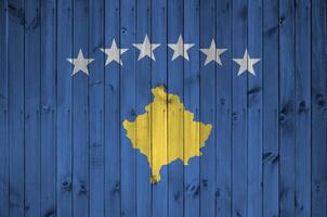 Kosovo bandera representado en brillante pintar colores en antiguo de madera pared. texturizado bandera en áspero antecedentes foto