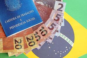 Brazilian work card and social security blue book and reais money bills on flag of Federative Republic of Brazil photo