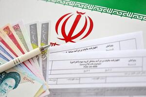 Iranian annual income tax return form F20-25-006 ready to fill on table with pen and iranian money on flag photo