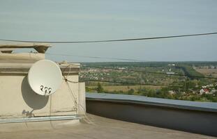 White satellite dish with three converters mounted on residental building rooftop concrete wall. Satellite television photo