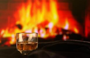 Whisky or whiskey or bourbon with ice on wooden surface on fireplace background. Luxury elite alcohol in wide glass. Low key scene photo