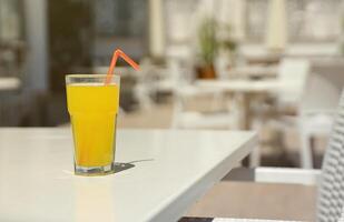 Glass of orange juice with plastic straw on white table in restaurant outdoor lounge zone photo