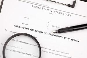 District court warrant for the arrest of a witness in a civil action papers on A4 tablet lies on office table with pen and magnifying glass photo