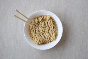 Bowl of instant cooking noodles with wooden chopsticks on white wooden table photo