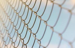 A photograph of a metal net used as a fence of private possessions. Old metal grid in perspective with a blurred background photo