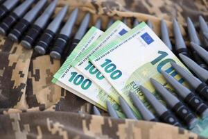 Bundles of euro bills and a machine gun belt on the camouflage uniform of a Ukrainian soldier. Concept of war financing, bribe or donation photo