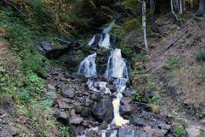 A mountain waterfall flows over the rocks. Waterfall cascade on mossy rocks photo