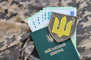 Symbol of Ukrainian army and military ID with bunch of money on the camouflage uniform of a Ukrainian soldier. Concept of payment to military personnel or bribe for deferment from service photo