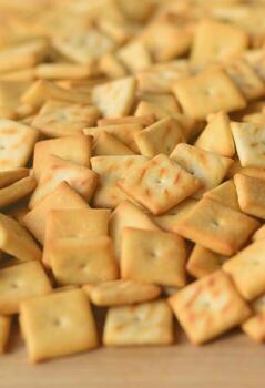 A lot of small cookies are square shaped. A pattern of a yellow salt cracker. Background image with salted pastry photo