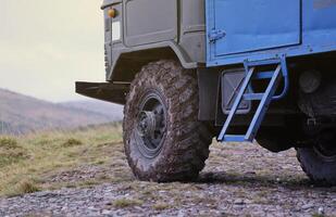 Wheel closeup in a countryside landscape with a mud road. Off-road 4x4 suv automobile with ditry body after drive in muddy road photo