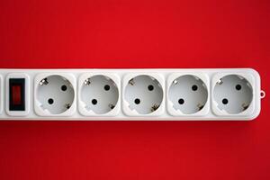 White electrical multi plug extender with european socket on bright red background photo