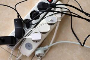 Overloaded power boards. Power strips with different electrical plugs on white floor photo