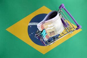 Brazilian money bills in small shopping cart on Brazilian flag photo