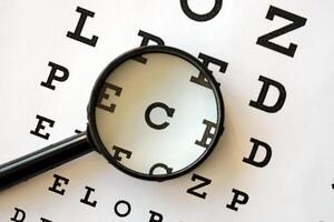 Magnifier glass focuses eye chart letters clearly and lies on eye test chart paper photo