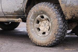 Wheel closeup in a countryside landscape with a mud road. Off-road 4x4 suv automobile with ditry body after drive in muddy road photo