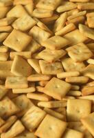 A lot of small cookies are square shaped. A pattern of a yellow salt cracker. Background image with salted pastry photo
