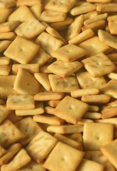 A lot of small cookies are square shaped. A pattern of a yellow salt cracker. Background image with salted pastry photo