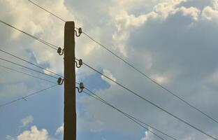 Old wooden electric pole for transmission of wired electricity on a background of a cloudy blue sky. Obsolete method of supplying electricity for later use photo