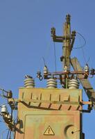 Old and obsolete electrical transformer against the background of a cloudless blue sky. Device for distribution of supply of high-voltage energy photo