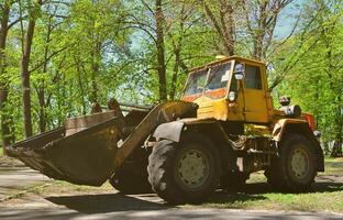 el equipo de mejora de la ciudad quita las hojas caídas en el parque con una excavadora y un camión. trabajo estacional regular en la mejora de los lugares públicos para la recreación foto