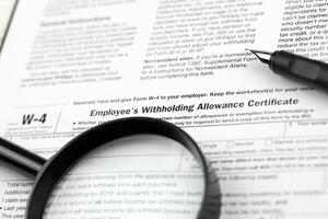 IRS Form W-4 Employee's withholding allowance certificate blank on A4 tablet lies on office table with pen and magnifying glass photo