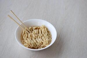 Bowl of instant cooking noodles with wooden chopsticks on white wooden table photo