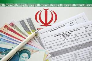 Iranian annual income tax return form F20-25-006 ready to fill on table with pen and iranian money on flag photo