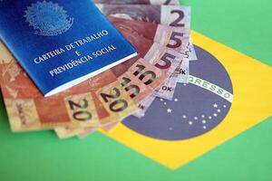 Brazilian work card and social security blue book and reais money bills on flag of Federative Republic of Brazil photo