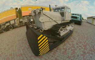 Photo of a gray bulldozer among the railway trains. Strong distortion from the fisheye lens