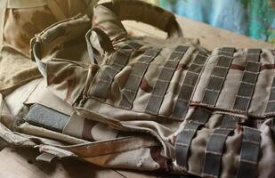 A military helmet of a Ukrainian soldier with a heavy bulletproof vest on wooden table in checkpoint dugout photo