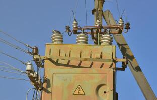 Old and obsolete electrical transformer against the background of a cloudless blue sky. Device for distribution of supply of high-voltage energy photo