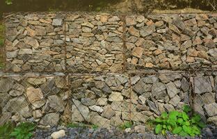Photo of several gabions. The mesh cells of the cubic form are filled with mountain stones of various shapes that let water through the rain, but protect the road from falling stones
