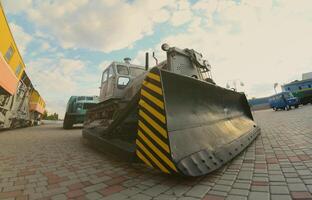 Photo of a gray bulldozer among the railway trains. Strong distortion from the fisheye lens