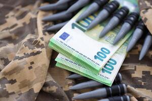 Bundles of euro bills and a machine gun belt on the camouflage uniform of a Ukrainian soldier. Concept of war financing, bribe or donation photo