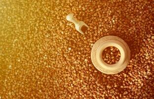 Background image of a large pile of buckwheat, in the middle of which lies a small jug and a wooden spatula for cereals photo