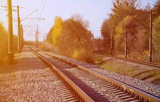 Autumn industrial landscape. Railway receding into the distance among green and yellow autumn trees photo