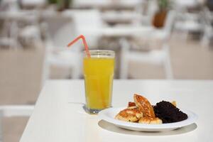 Glass of orange juice with plastic straw on white table in restaurant outdoor lounge zone photo