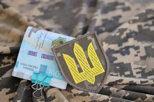 Ukrainian army symbol and bunch of hryvnia bills on military uniform. Payments to soldiers of the Ukrainian army, salaries to the military photo