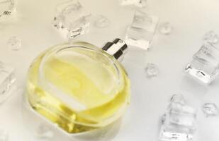 frasco amarillo de perfume femenino, fotografía objetiva del frasco de perfume en cubitos de hielo y agua sobre una mesa blanca. vista desde arriba. foto de producto de maqueta, concepto de frescura