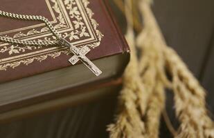 Silver necklace with crucifix cross on christian holy bible book on black wooden table. Asking blessings from God with the power of holiness photo