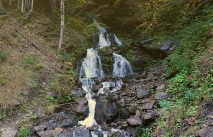 A mountain waterfall flows over the rocks. Waterfall cascade on mossy rocks photo