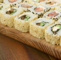 Close-up of a lot of sushi rolls with different fillings lie on a wooden surface. Macro shot of cooked classic Japanese food with a copy space photo