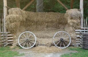 Place with stacks of hay cubes and rustic wooden wheels of old cart photo