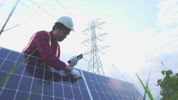 ingegneria nel standard sicurezza uniforme Lavorando ispezionare il elettricità alto voltaggio polo con tavoletta vicino Torre con elettricità. video