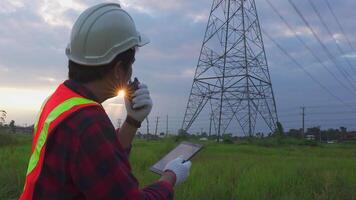 Ingenieurwesen im Standard Sicherheit Uniform Arbeiten prüfen das Elektrizität hoch Stromspannung Pole mit Tablette in der Nähe von Turm mit Elektrizität. video